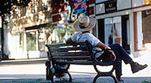 man in strawhat sitting on sidewalk bench